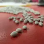 Close-up of white polymer pellets on a red industrial surface, representing recycled plastic material used in polymer production.