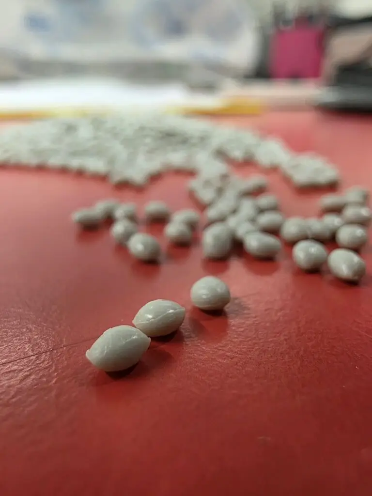 Close-up of white polymer pellets on a red industrial surface, representing recycled plastic material used in polymer production.